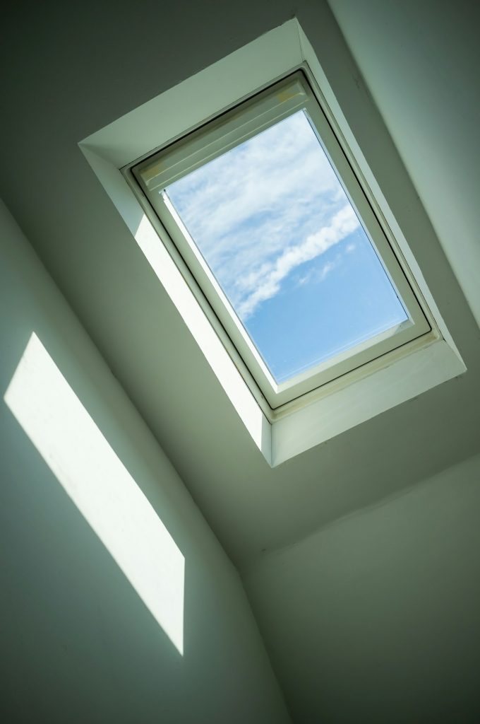 Closed roof window through which you can see the blue sky and white clouds on sunny day. Bottom view