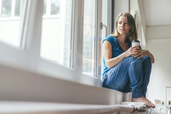 Smiling young woman holding takeaway coffee sitting at the window